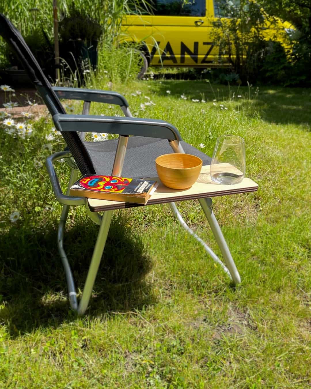 Holzablage mit einem Buch, Schale und Glas an einem faltbaren Campingstuhl